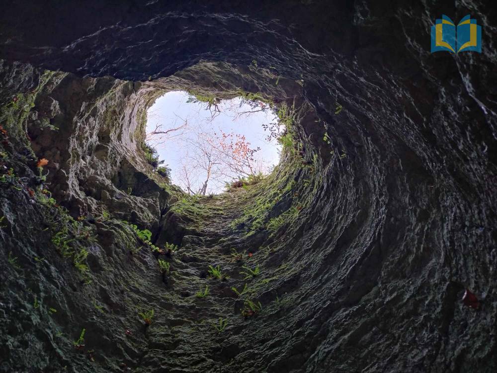 Zdjęcie: Wnętrze jaskini, w kształcie komina, z dużym otworem, w kształcie serca. Zdjęcie z dołu jaskini.